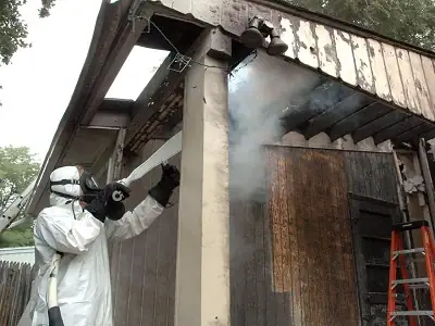 Technician in a protective suit spraying a ceiling