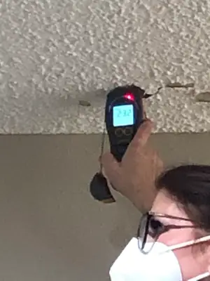 Technician in a mask checking a ceiling with a meter