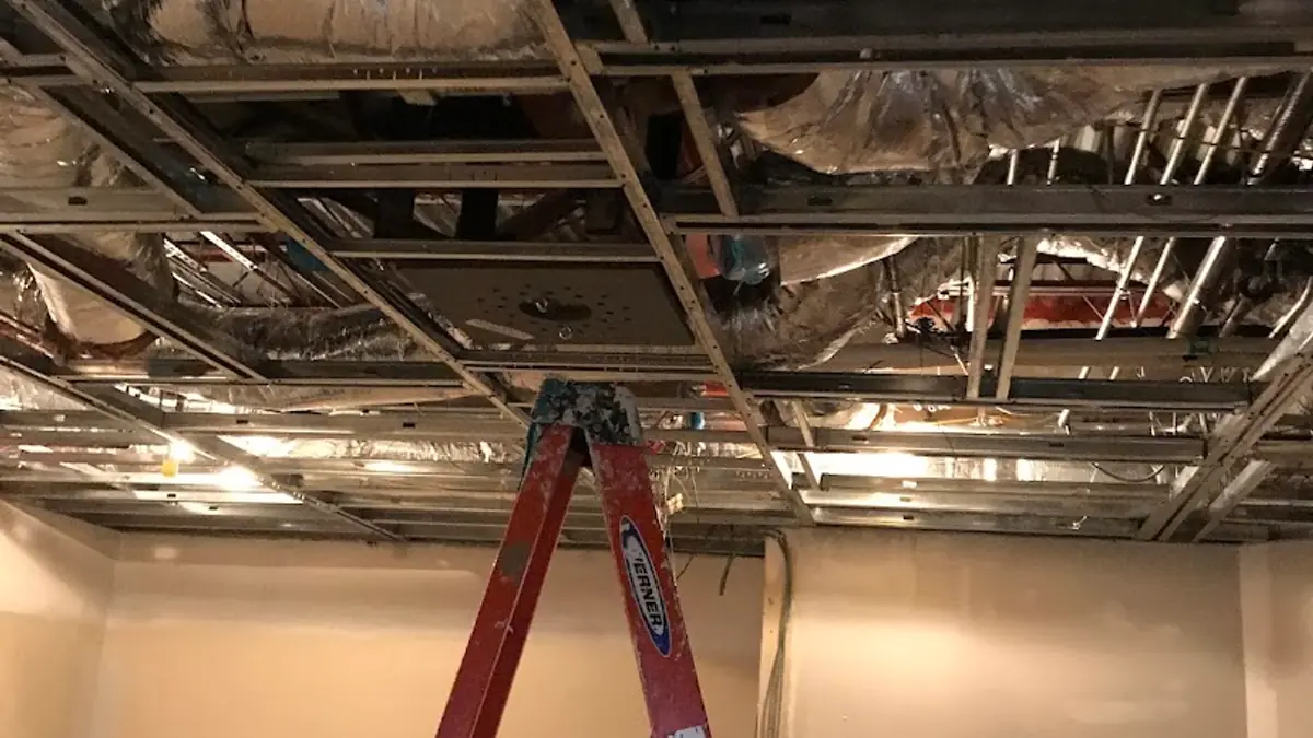 Commercial interior stripped to the ceiling deck with a worker on a ladder