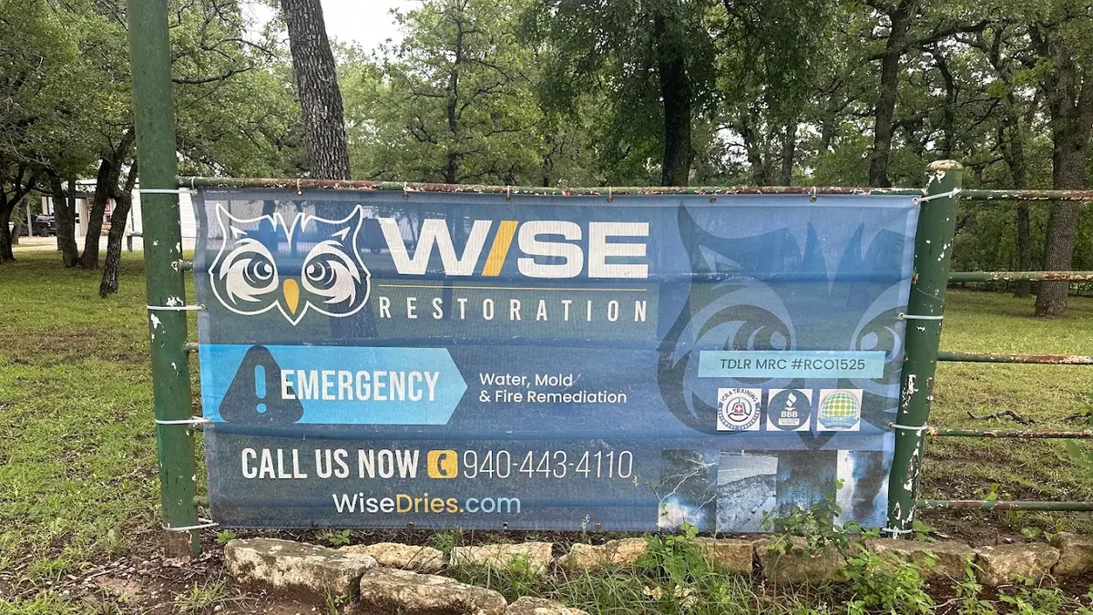 Wise Restoration Inc banner on a fence at a job site